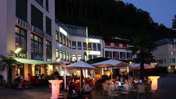 Abendliche Stimmung vor der Brasserie Burg in Vaduz mit beleuchteter Terrasse und Gästen unter Sonnenschirmen.