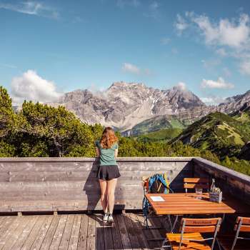 Wanderin blickt von Holzterrasse bei der Aussichtsterasse auf ein beeindruckendes Alpenpanorama.