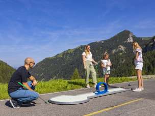 Familie geniesst eine Partie Minigolf im sonnigen Malbun in Liechtenstein, umgeben von grüner Alpenlandschaft und Bergen im Sommer.