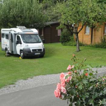 Wohnmobilstellplatz auf dem Campingplatz Mittagsspitze mit grüner Wiese und umgebenen Holzhütten.