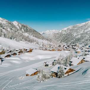 Luftaufnahme von Malbun im Winter mit verschneiten Holzhäusern, eingebettet in die Alpenlandschaft Liechtensteins