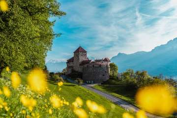 Schloss Vaduz umgeben von blühenden Frühlingswiesen und Bergen im Hintergrund – Liechtensteins Wahrzeichen in voller Pracht