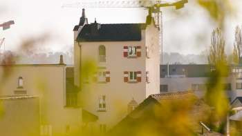 Nahaufnahme des historischen Turms des Rathauses Vaduz mit markanten roten Fensterläden, umgeben von Baustellenkränen im Hintergrund.