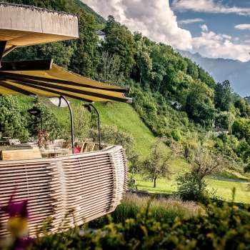 Sonnige Terrasse mit blühenden Blumen und elegant gedeckten Tischen mit Blick ins Tal