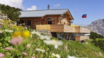Aussenanischt des Sareis Bergrestaurant mit Blumen im Vordergrund und Bergen im Hintergrund Aussenanischt des Sareis Bergrestaurant mit Blumen im Vordergrund und Bergen im Hintergrund