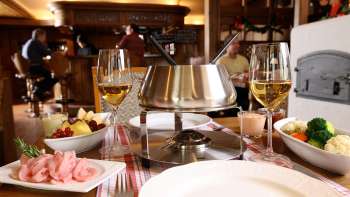 Nahaufnahme von Käsefondue-Set mit frischem Brot, Gemüse und Wein im stilvollen Ambiente