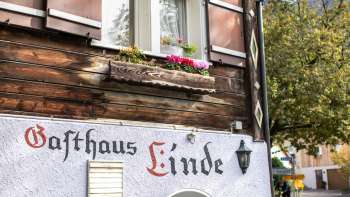 Fassade des Gasthaus Linde mit rustikalem Holzbau und Fensterläden, verziert mit Blumen.