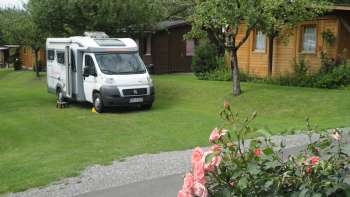 Wohnmobilstellplatz auf dem Campingplatz Mittagsspitze mit grüner Wiese und umgebenen Holzhütten.