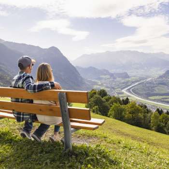 Zwei Wanderer sitzen auf einer Bank und geniessen die Aussicht auf das Rheintal