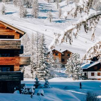 Gemütliche Chalets im Wintersportort Malbun umgeben von verschneiten Bäumen und Skipisten im Hintergrund