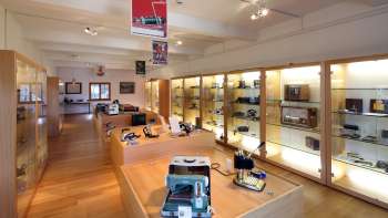 Blick in einen hellen Ausstellungsraum des Lawena Museums mit beleuchteten Vitrinen voller historischer Elektrogeräte.