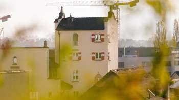 Nahaufnahme des historischen Turms des Rathauses Vaduz mit markanten roten Fensterläden, umgeben von Baustellenkränen im Hintergrund.
