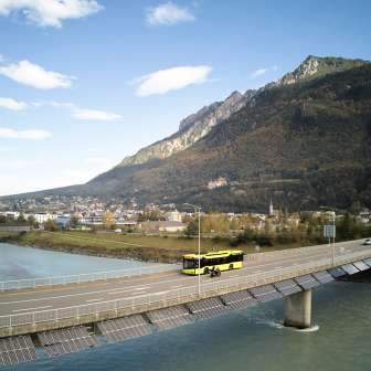 Gelber LIEmobil Bus überquert die Rheinbrücke bei Vaduz mit Bergpanorama im Hintergrund – Liechtenstein erleben