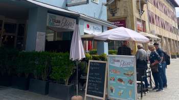 Außenansicht des Restaurants Elisas mit Sonnenschirmen und Speisekarte auf der Tafel Außenansicht des Restaurants Elisas mit Sonnenschirmen und Speisekarte auf der Tafel