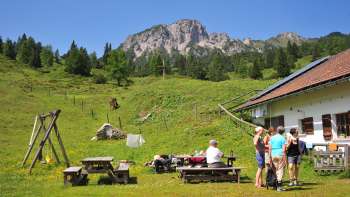 Blick auf die Berge von der Alpe Guschg an der mehrere Personen Pause machen und genießen