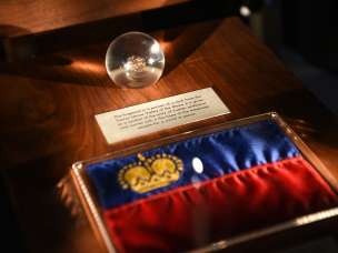 Ausstellungsstück in der Schatzkammer Liechtenstein: Liechtensteiner Flagge mit goldener Krone und gläserne Kugel mit historischem Fundstück