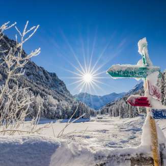 Verschneite Wegweiser und traumhafte Winterlandschaft bei strahlendem Sonnenschein in Steg, Liechtenstein.