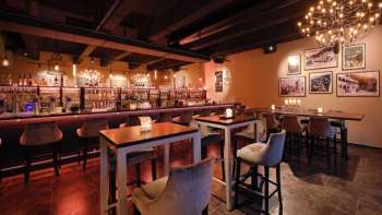 Elegantes Restaurant-Interieur mit dunklen Holzelementen, Barbereich und bequemen Stühlen in einem gemütlichen Ambiente.