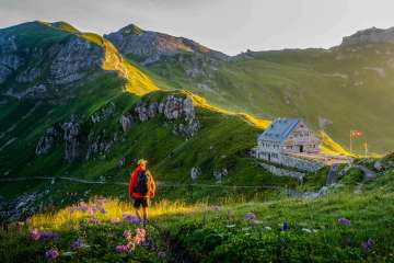 Wanderer blickt auf die Pfälzerhütte in Liechtenstein, umgeben von grüner Berglandschaft und Alpenpanorama bei Abendlicht