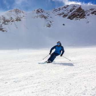 Skifahrer auf breiter Skipiste in Malbun, Liechtenstein, umgeben von verschneiten Alpenhängen und strahlend blauem Himmel