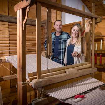 Ein Paar betrachtet einen funktionstüchtigen historischen Webstuhl im Walsermuseum Triesenberg in Liechtenstein, umgeben von Holzvertäfelung