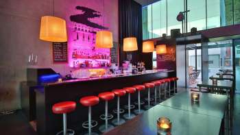 Moderne Bar mit langen Tresen, roten Barhockern und stilvoller Beleuchtung in Pink und Orange