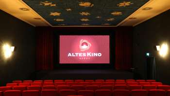 Kinosaal des Alten Kino Vaduz mit roten Kinosesseln, einer Bühne mit rotem Vorhang und einer blauen Decke mit goldenen Sternenmotiven.