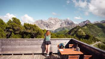 Eine Frau geniesst die Aussicht von der Aussichtsterrasse Sareis auf die Liechtensteiner Alpen und das Rheintal bei klarem Wetter