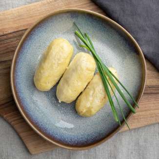 Drei Hafalääb-Knödel auf einem Teller mit Schnittlauchgarni, serviert auf einem Holzbrett – traditionelle Speise aus Liechtenstein
