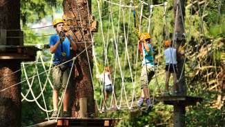 Kinder und Jugendliche mit Helmen im Hochseilgarten des Seilparks Triesen in Liechtenstein, gesichert auf Kletterelementen im Wald