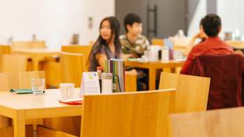 Gäste sitzen an Holztischen im Café im Kunstmuseum, plaudern entspannt und genießen die Atmosphäre.
