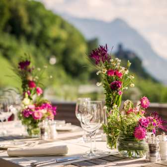 Elegant gedeckter Tisch mit Blumenarrangements auf einer Terrasse mit Alpenblick – perfekte Kulisse für Feiern oder romantische Dinner in Liechtenstein