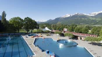 Gesamtansicht des Freibads Mühleholz mit mehreren Becken und herrlichem Alpenpanorama im Hintergrund.