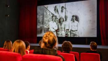 Besucher sitzen in einem roten Kinosaal im alten Kino in Vaduz und schauen einen historischen Film über Liechtenstein