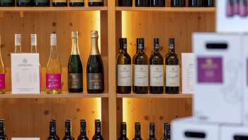 Innenraum der Hofkellerei mit stilvoll beleuchteten Holzregalen voller Weinflaschen und Kartons.