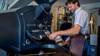 Mann röstet Kaffeebohnen an einer modernen Röstmaschine in einer Kaffeerösterei Mann röstet Kaffeebohnen an einer modernen Röstmaschine in einer Kaffeerösterei