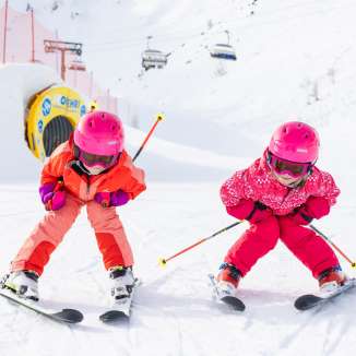 Zwei Kinder mit pinken Helmen fahren lachend Ski auf der Piste in Malbun im sonnigen Winterwetter.