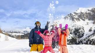 Familie geniesst gemeinsam den Schnee in Malbun – Kinder werfen fröhlich Schneebälle vor winterlicher Bergkulisse.