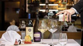 Kellner schenkt Weißwein zu einem elegant angerichteten Tellergericht im Restaurant Alpspitz ein.