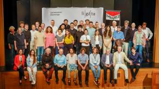Gruppenfoto der Teilnehmenden und Dozent:innen der Liechtensteiner Gitarrentage (LiGiTa) auf einer Bühne vor einem Banner mit Veranstaltungslogo
