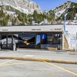 Eingang des Malbun Centers mit Touristeninformation und Restaurant vor schneebedeckter Berglandschaft in Malbun, Liechtenstein