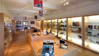 Blick in einen hellen Ausstellungsraum des Lawena Museums mit beleuchteten Vitrinen voller historischer Elektrogeräte.