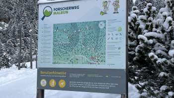 Mädchen mit grünem Hut blickt durch ein Fernrohr auf dem Forscherweg Malbun mit Panorama-Ausblick auf die Liechtensteiner Alpen.