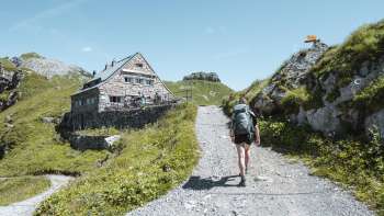 Wanderin mit Rucksack geht auf einem Bergpfad auf die Pfälzerhütte in den Liechtensteiner Alpen zu