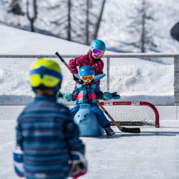 Familie beim Schlittschuhlaufen in Malbun, Kind sitzt auf einer Eislaufhilfe in Tierform.