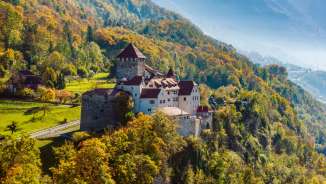 Schloss Vaduz auf einem bewaldeten Hügel in herbstlicher Landschaft in Liechtenstein