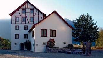 Historisches Gebäudeensemble der Pfrundbauten mit Fachwerkfassade und Bergkulisse in Liechtenstein bei Abendlicht.