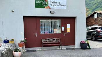 Eingang zum Hofladen Aeulehof mit rotem Tor, Sitzbank und Blumendekoration in Triesen, Liechtenstein.