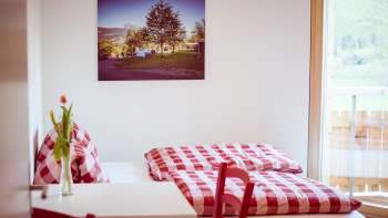 Gemütliches Doppelzimmer im Gästehaus beim Camping Mittagsspitze mit rot-weiß karierter Bettwäsche und Dekoration.