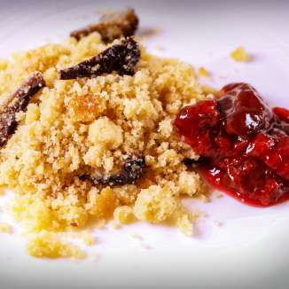 Traditionelles Riebelgericht aus Liechtenstein mit knusprigem Maisgrieß und süßem Zwetschgenröster auf einem weißen Teller serviert.